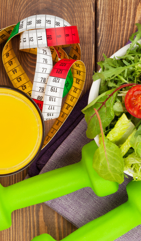 Салат из зелени на столе с соком и гантелями