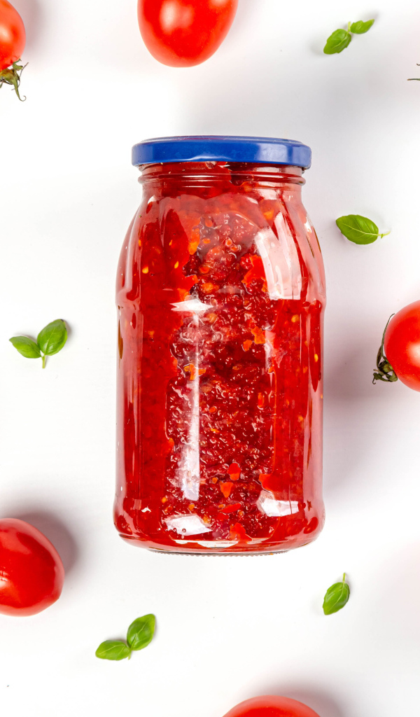 Банка аджики на белом фоне с помидорами