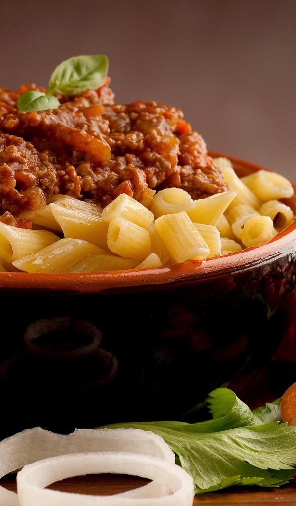 Макароны в миске с фаршем на столе с помидорами