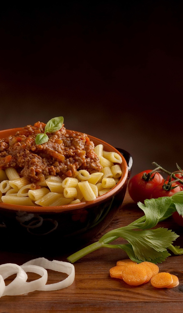 Макароны с фаршем на столе с бокалом вина и помидорами