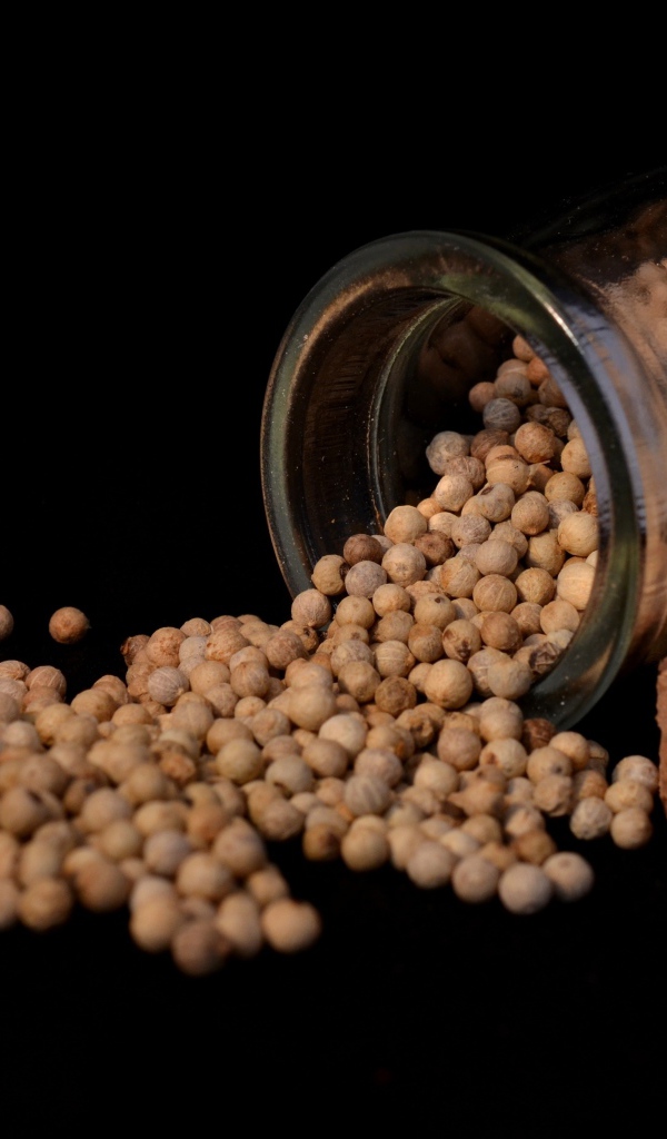 Перец горошек в стеклянной банке на черном фоне 