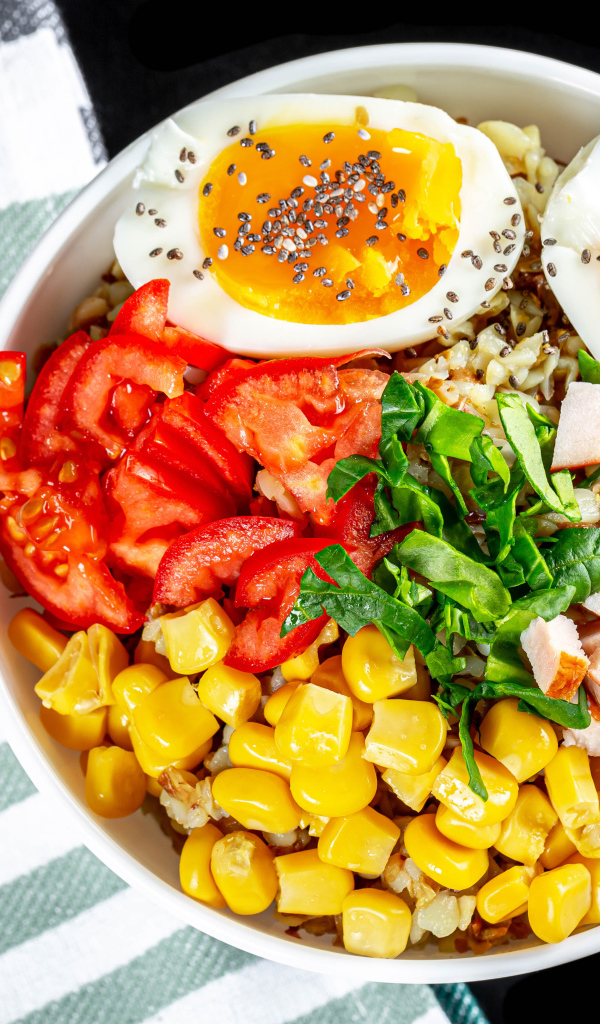 Каша в тарелке с помидорами, кукурузой, ветчиной и яйцом