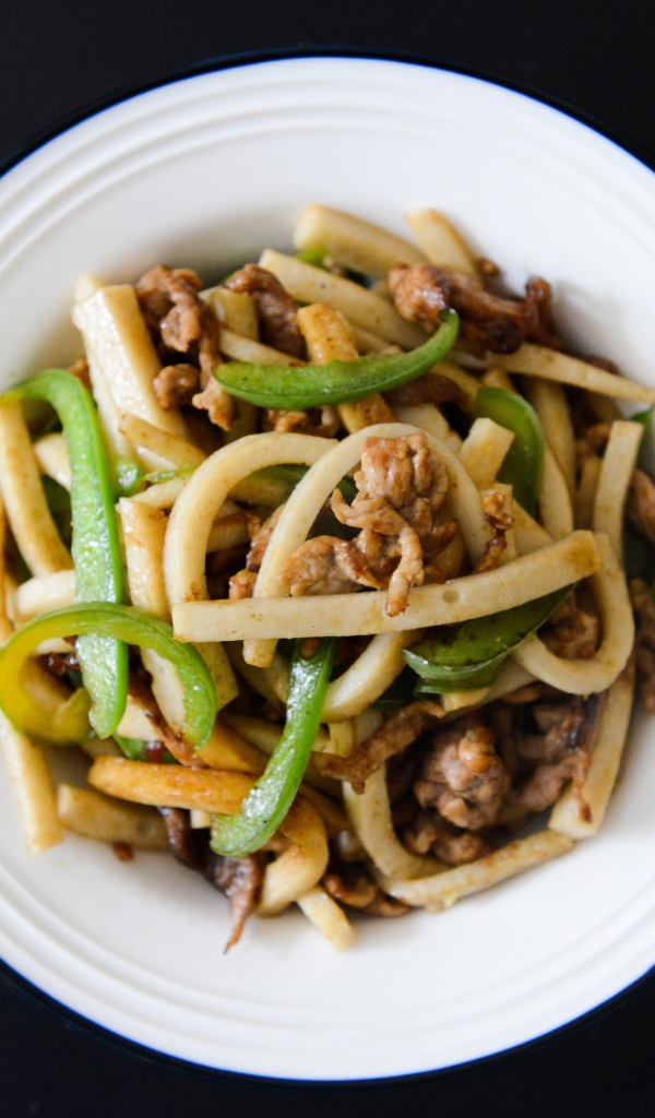 Салат с мясом в белой тарелке на черном фоне