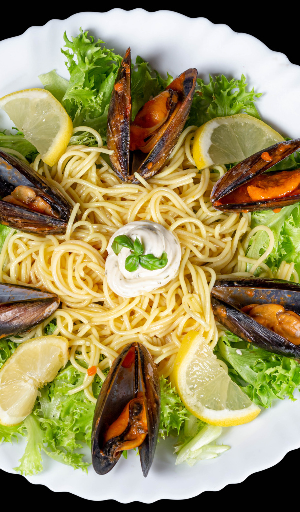 Спагетти с мидиями и листьями салата на белой тарелке