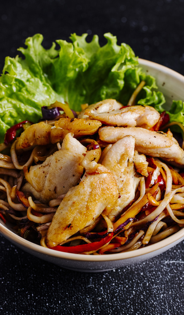 Спагетти с соусом в тарелке с кусочками курицы и листьями салата