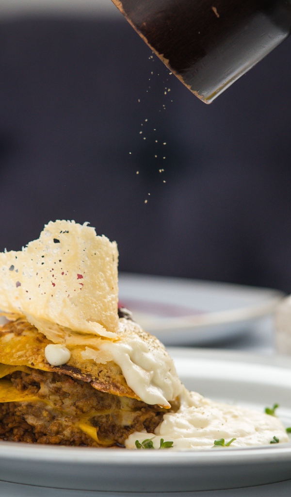 Кусок лазаньи посыпают перцем 