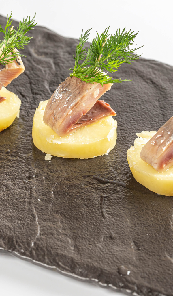 Три куска вареного картофеля с сельдью и укропом