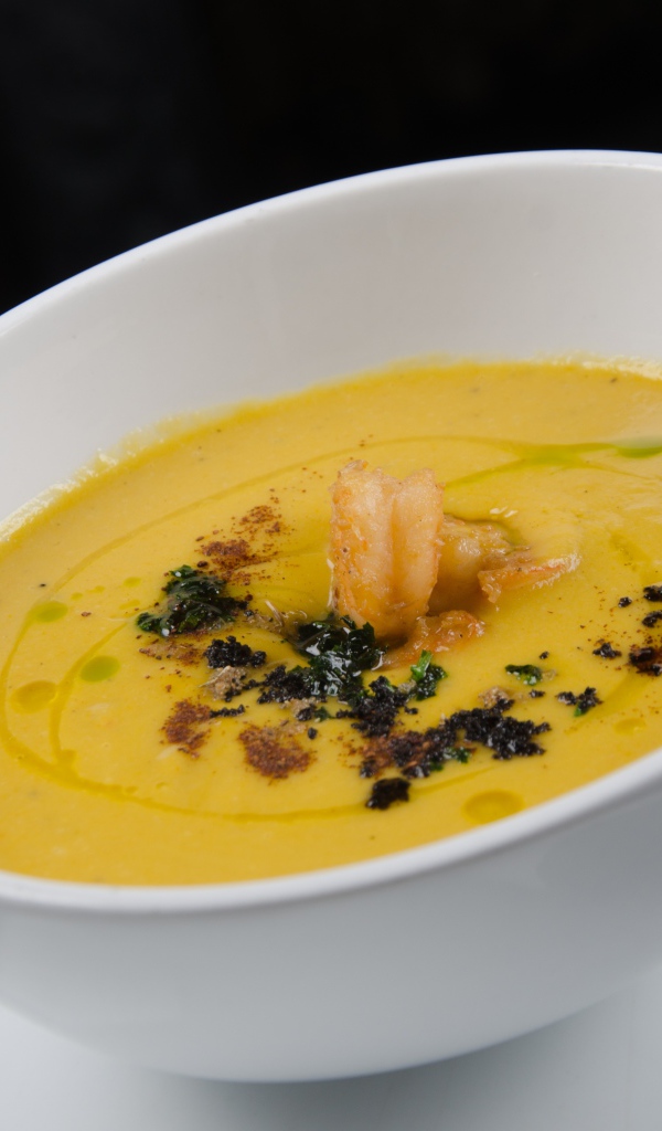 Желтый суп пюре в белой тарелке на черном фоне