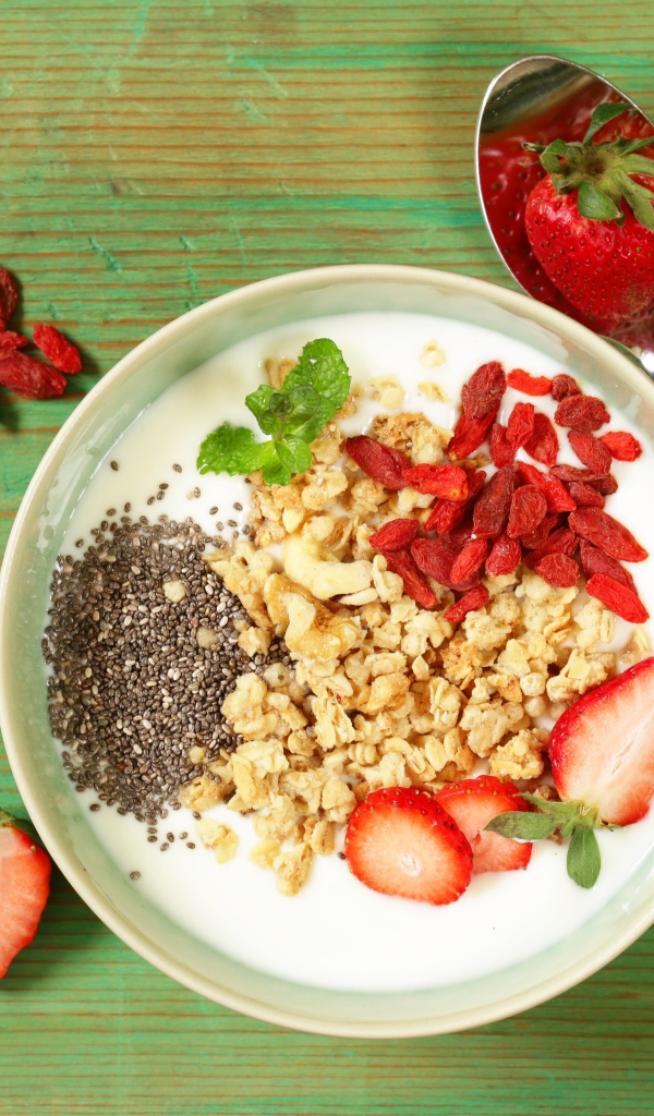 Йогурт с сухофруктами и клубникой на столе в миске 