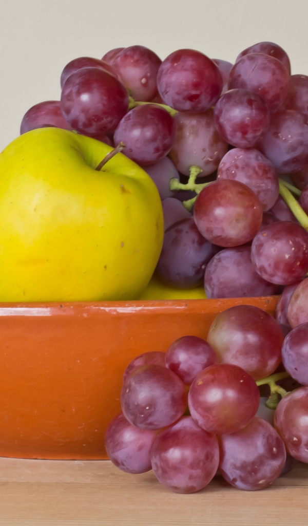 Яблоки и розовый виноград в тарелке на столе 