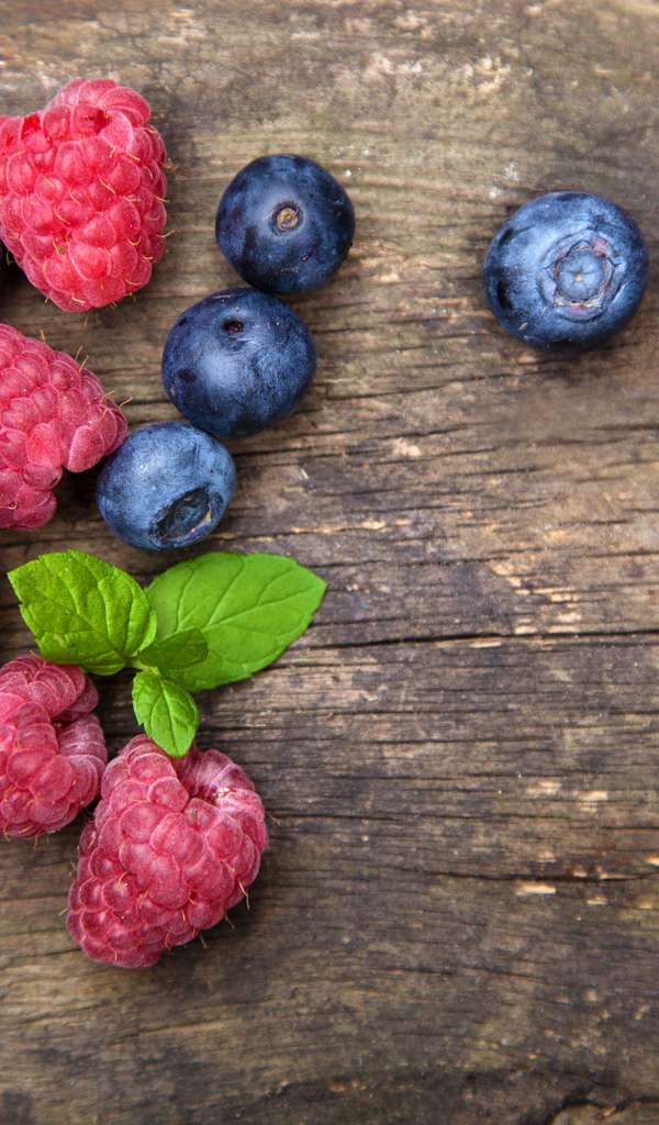 Голубые ягоды черники и красные ягоды малины на деревянном столе