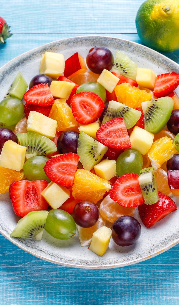 Вкусный салат из свежих овощей и ягод на голубом столе