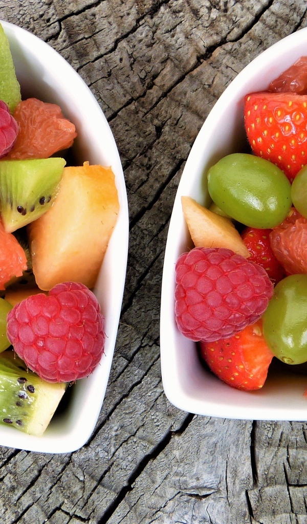 Салат из фруктов и ягод в белой тарелке на деревянном столе