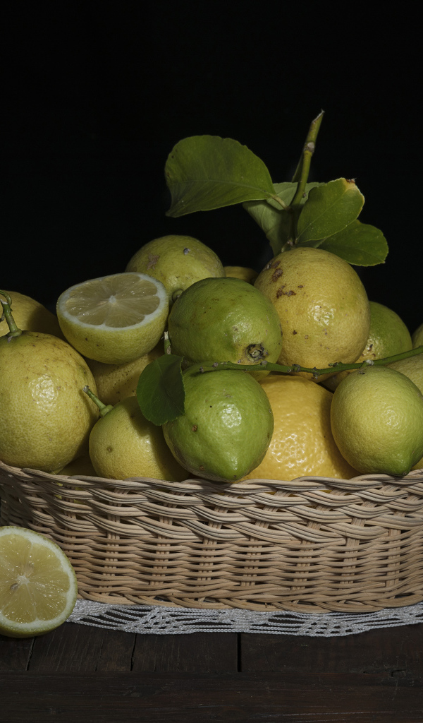 Lemons and limes in a wicker basket on a black background