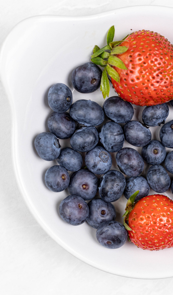 Много синей черники с клубникой в белой тарелке 