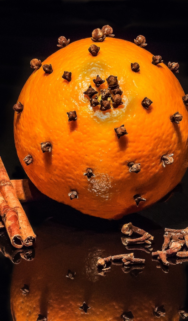 Оранжевый апельсин с гвоздикой и корицей на черном фоне 