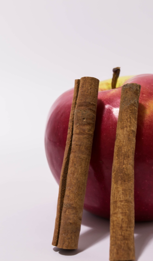 Красное яблоко с палочками корицы на сером фоне