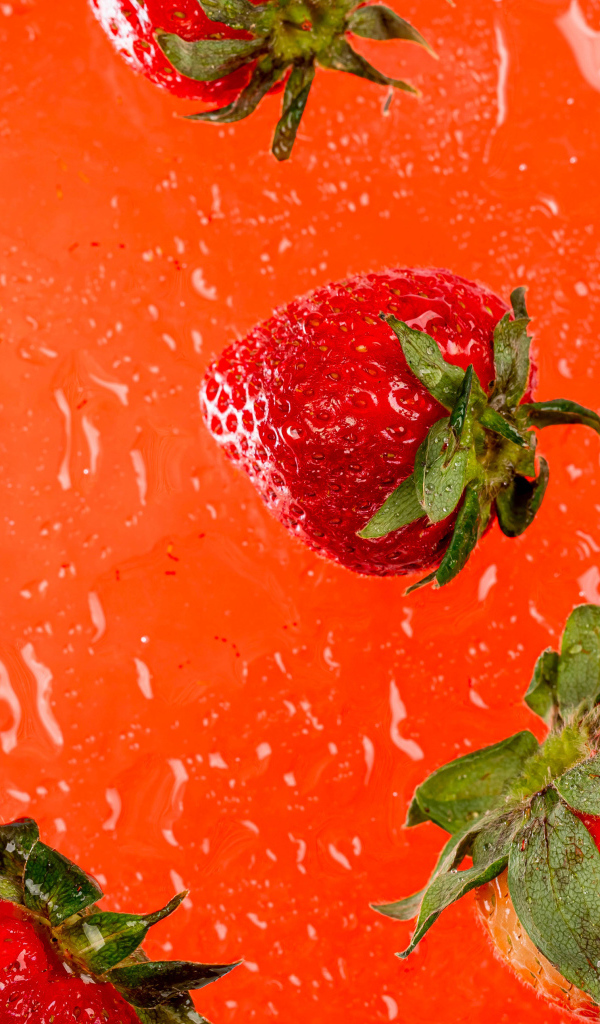 Красная клубника в воде на оранжевом фоне 