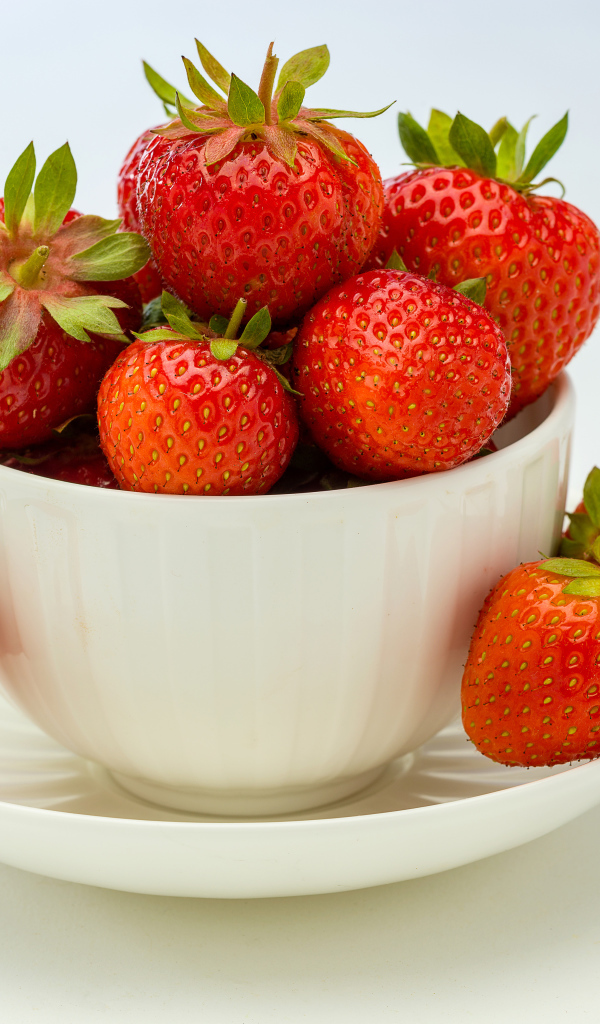 Спелая красная клубника в белой миске с блюдцем