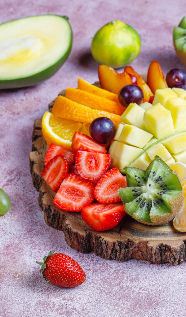 Нарезанные фрукты и ягоды на деревянной доске 