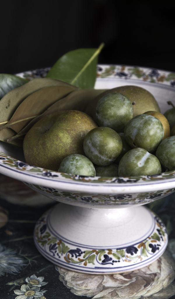 Белые сливы и зеленые яблоки в вазе на столе 