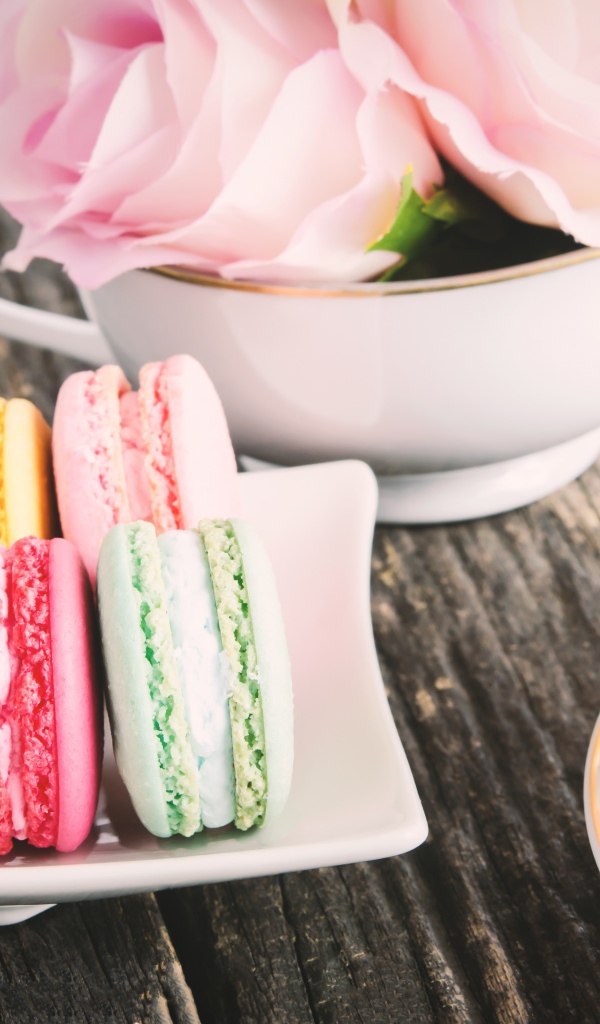 Десерт макарон на столе с чаем и цветами розы