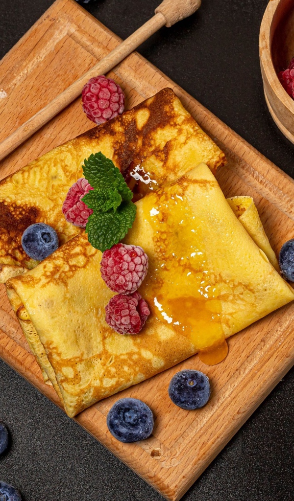 Блины с медом и ягодами черники и малины на черном столе 