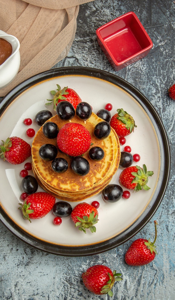 Оладьи с ягодами клубники и винограда на столе с медом