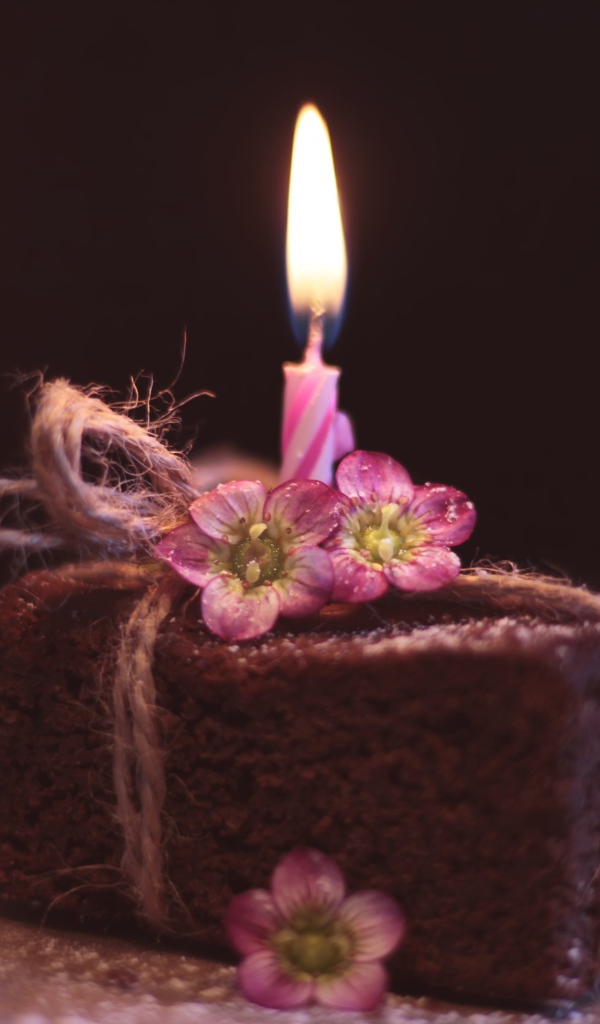 Кусок торта на столе с розовыми цветами и свечкой