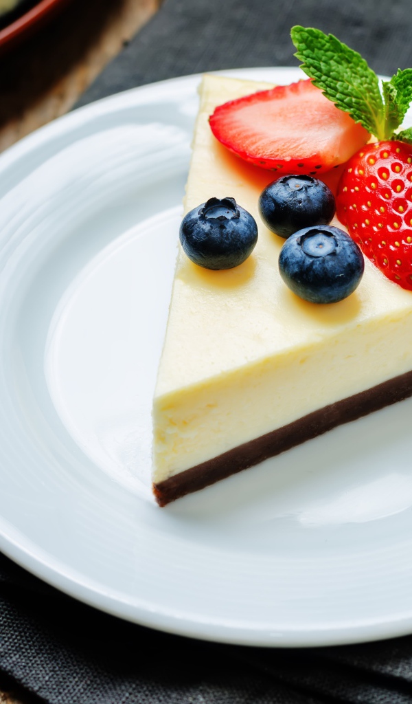 Кусок чизкейка на белой тарелке с клубникой и черникой 