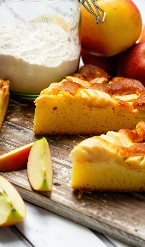 Куски пирога на столе с яблоками и мукой