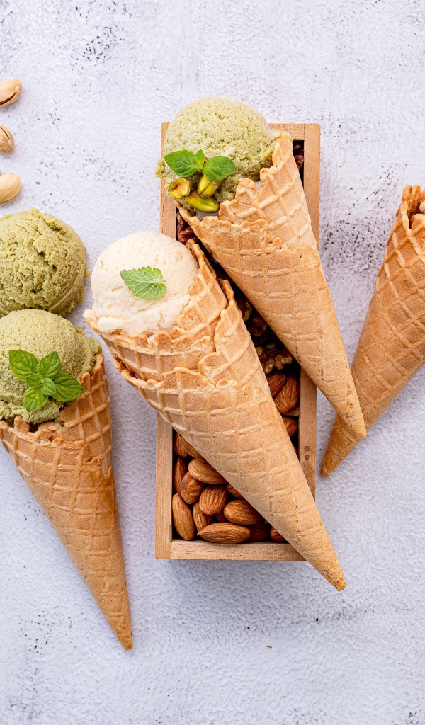 Вафельные рожки на столе с фисташковым мороженым и миндалем 