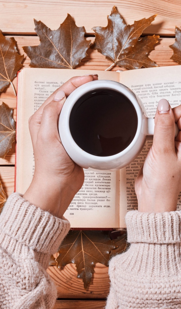 Чашка кофе в руках на столе с книгой и листьями