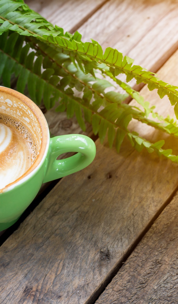 Чашка вкусного капучино  на столе с листьями папоротника