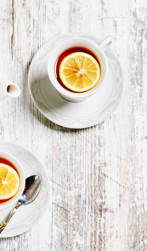 Две чашки чая с лимоном на столе с белым чайником