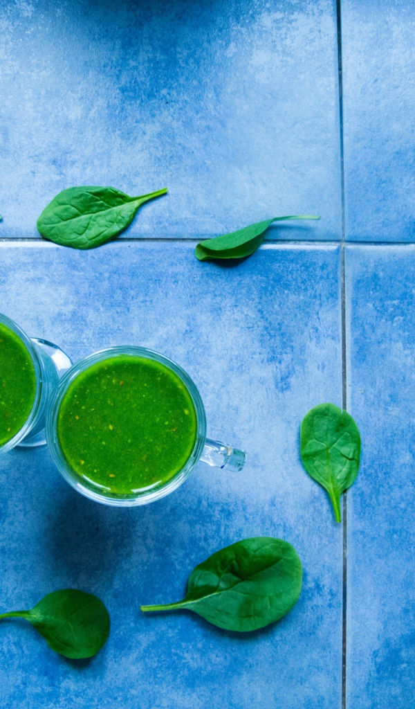 Два зеленых смузи с листьями базилика на голубом фоне