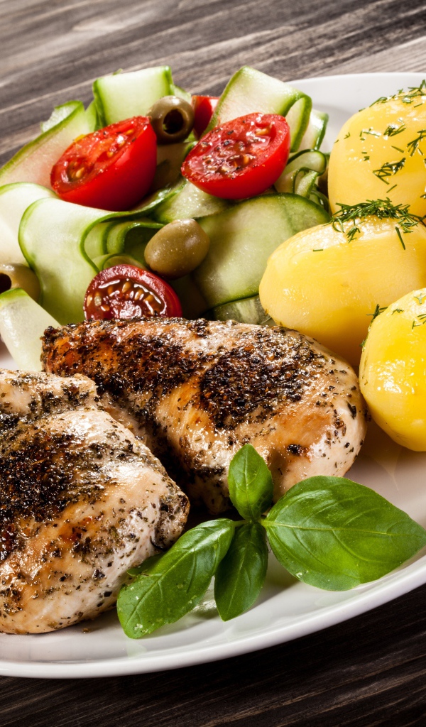 Куски курицы на тарелке с картофелем, помидорами и кабачком 