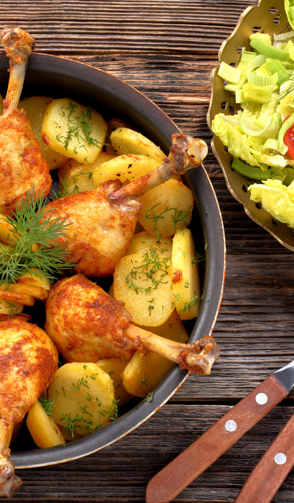 Fried chicken legs with potatoes on a table with salad