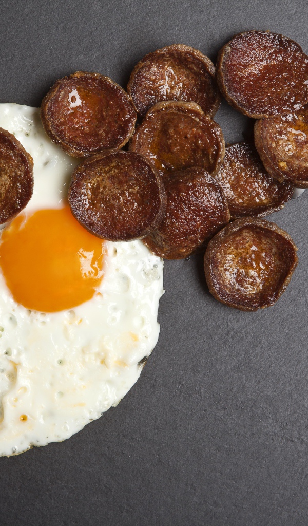 Жареная колбаса с яичницей глазуньей на сером столе 