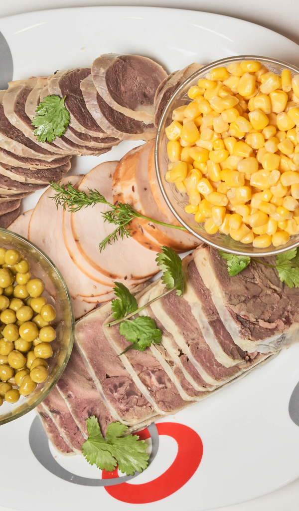Meat products on a plate with corn and green peas