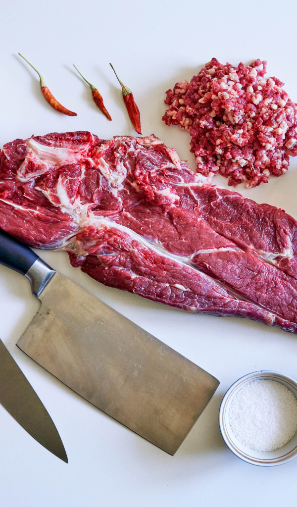 Кусок мяса со специями и ножами на столе 