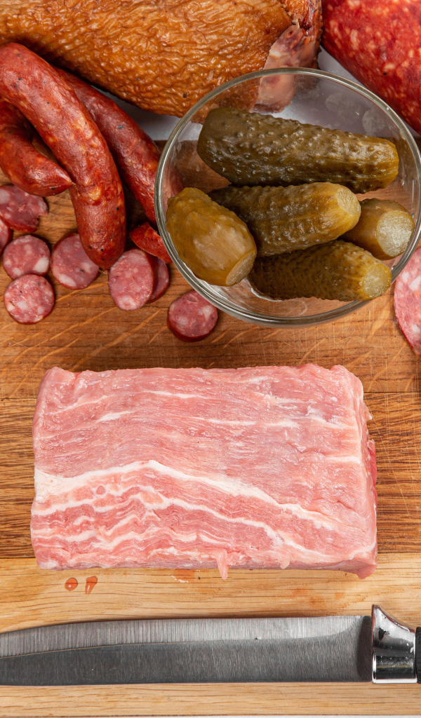 Колбаса на столе с огурцами, помидорами и зеленью 