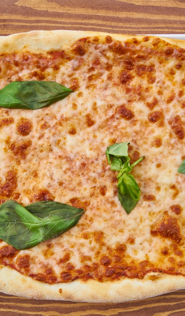 Пицца с сыром и листьями базилика на столе со столовыми приборами