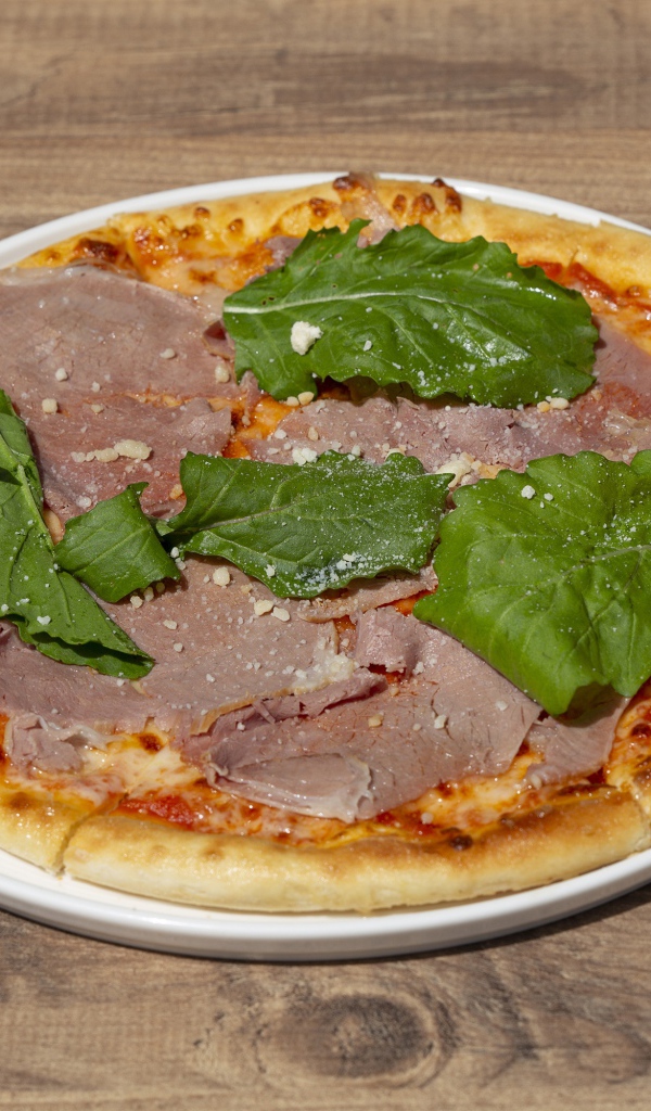 Пицца с кусочками мяса и зеленью на столе