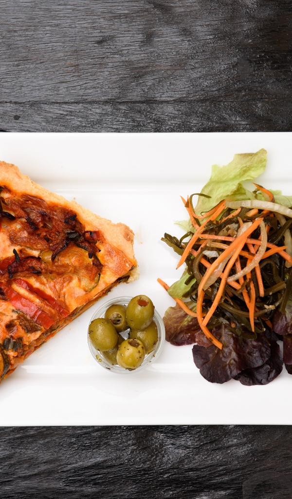 Кусок пиццы с салатом и оливками на белой тарелке