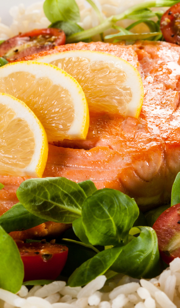 Кусок запеченной красной рыбы на тарелке с лимоном, рисом, базиликом и помидорами