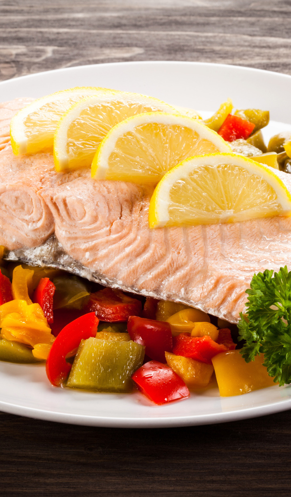 Кусок рыбы на тарелке с овощами и лимоном