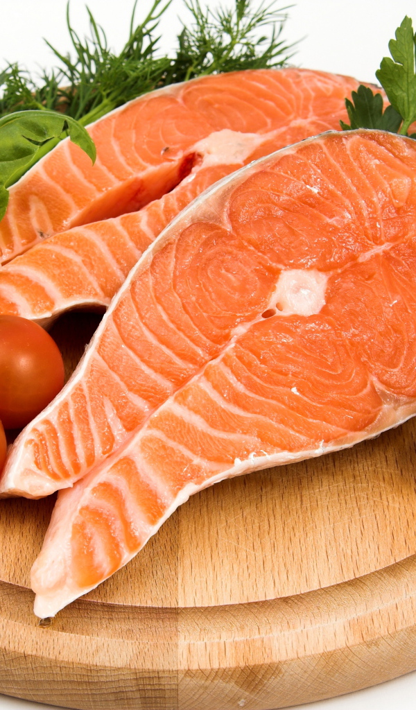 Два куска красной рыбы на доске с зеленью и помидорами