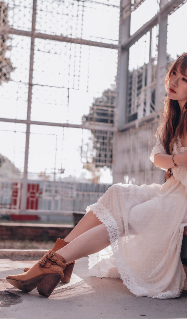 Красивая девушка азиатка в белом платье сидит на лавочке