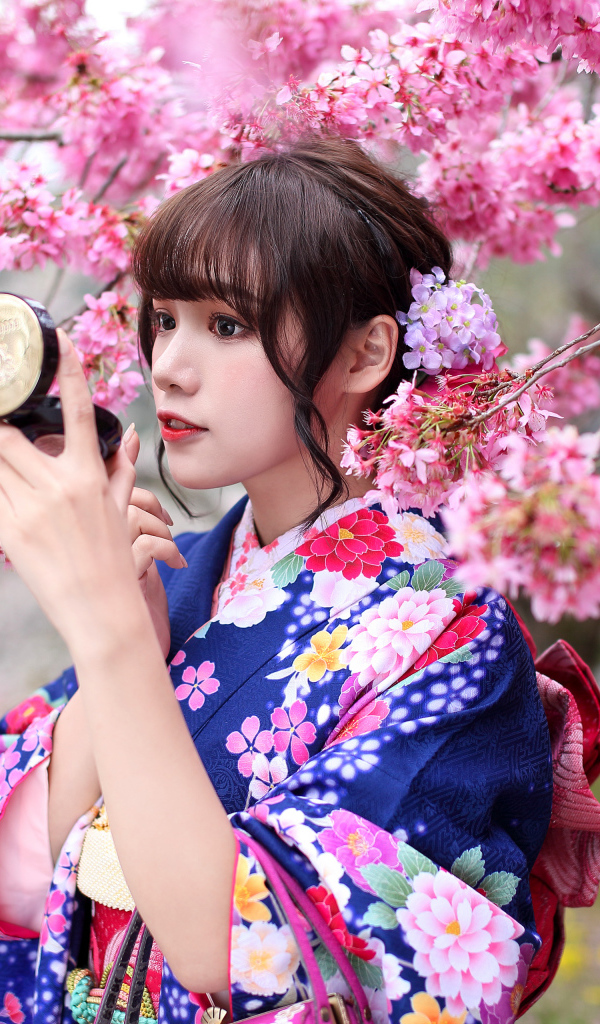 Девушка в кимоно стоит у куста сакуры